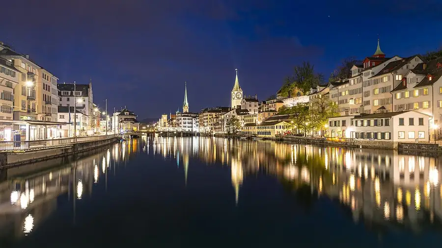 Stand-up comedy in Switzerland: Zurich at night, the old town's lights and church spires reflected in the Limmat
