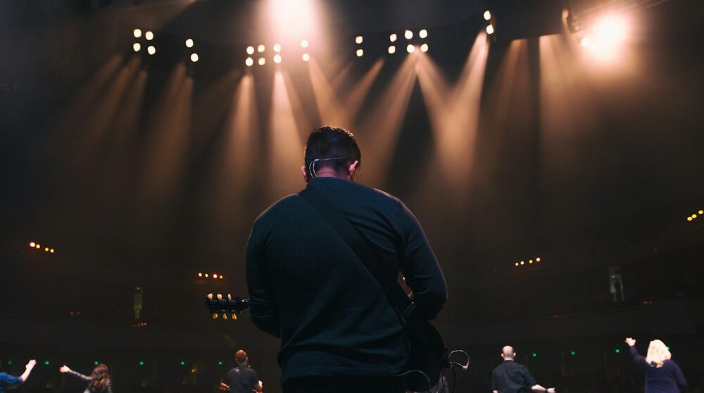 Tools for comedians, from the other side of the mic: a performer seen from behind, facing warm stage lights and a crowd