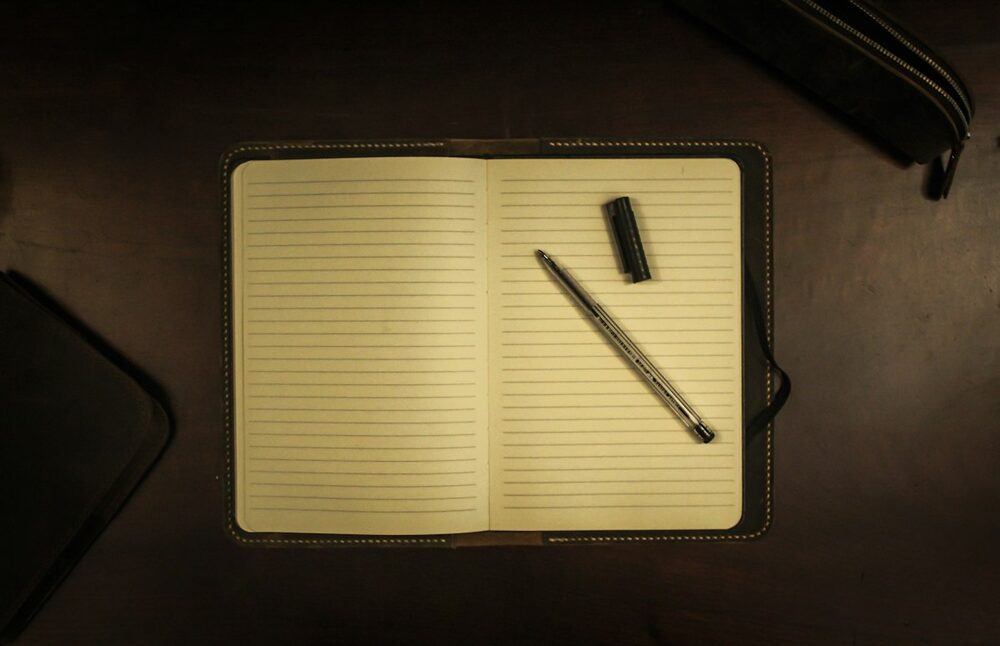 An open lined notebook and a pen on a dark desk, ready for comedy questions and their answers
