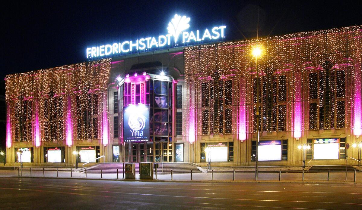 Stand-up comedy in Germany: the Friedrichstadt-Palast on Friedrichstraße in Berlin at night, its name lit in white above a front hung with warm lights, home of the Quatsch Comedy Club Berlin