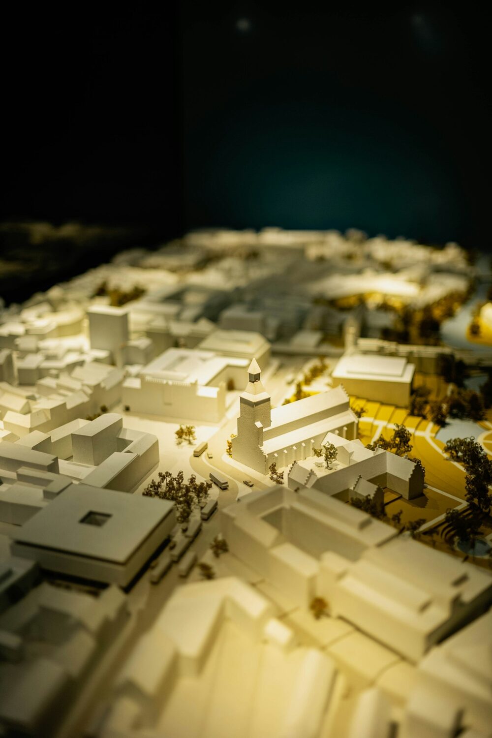 The world pay-to-play comedy sells: a white scale model of a town under warm light in the dark, a mock-up rather than the real place