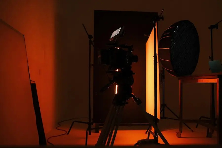 A film studio in orange light: a camera on a tripod between a light panel and a softbox: SAG-AFTRA and stand-up