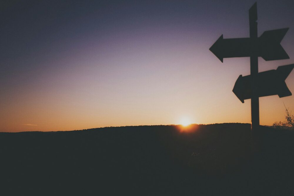 A comedy quiz with more than one road: a blank signpost silhouetted against a dusk sky, the sun on the ridge