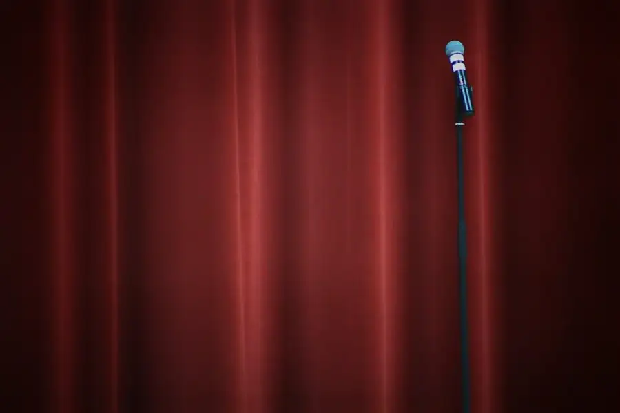 A lone microphone on a stand against a red club curtain: comedic timing