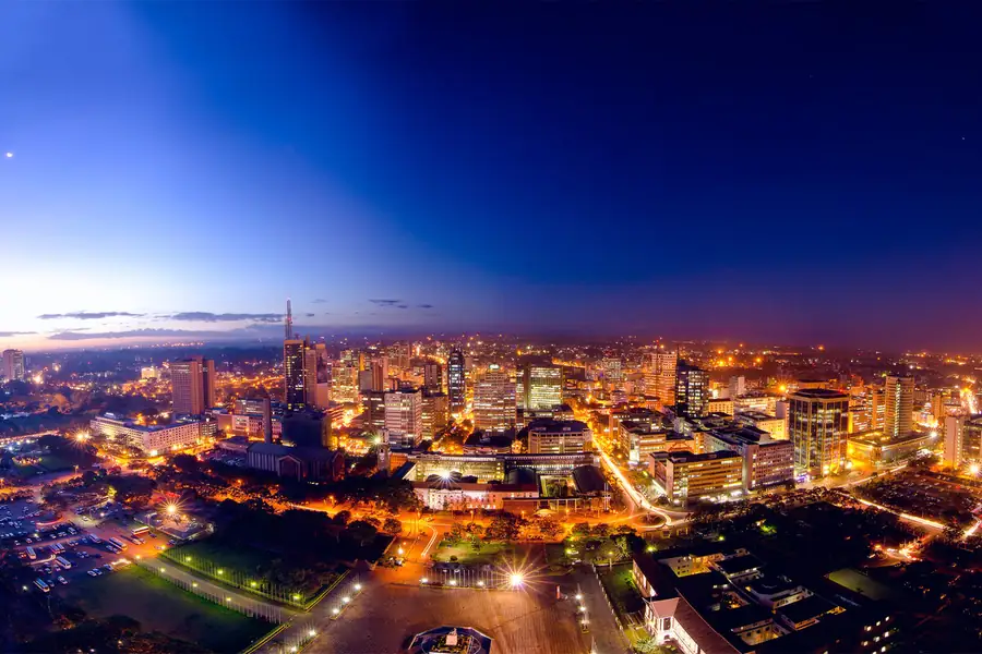 Stand-up comedy in Kenya: Nairobi's city centre at dusk, its towers and streets lit gold under a deep blue sky