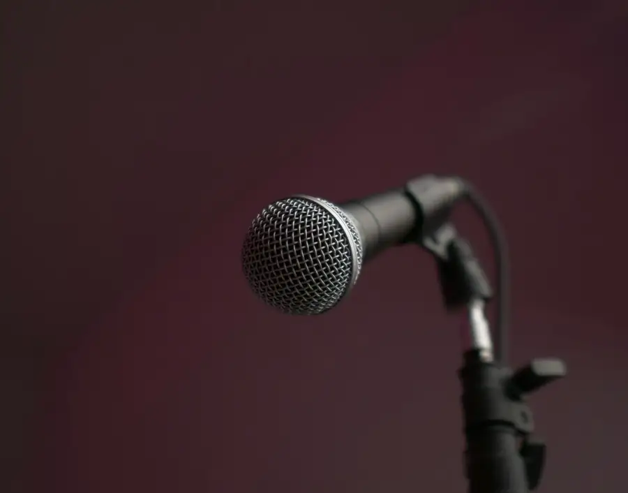 A microphone on a stand against a dark red wall, ready for the first set of a free course on how to start stand-up comedy