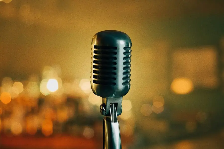 A vintage-style microphone on a stand, a warm bar blurred behind it: what comes after open mics