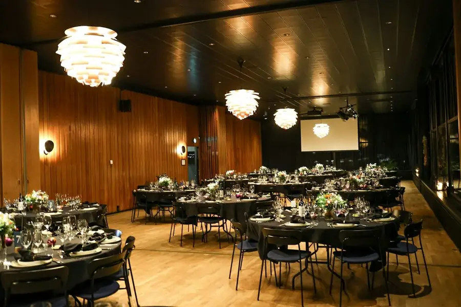 A wood-panelled function room set for a dinner, round tables and a screen at the far end: writing a clean comedy set