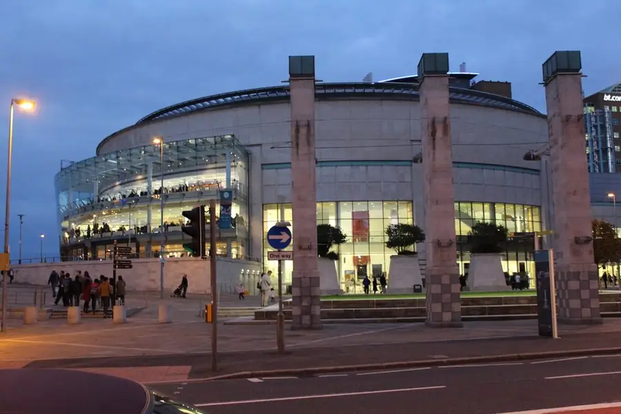 Waterfront Hall in Belfast at dusk: the round hall with its glass foyer lit and people arriving.