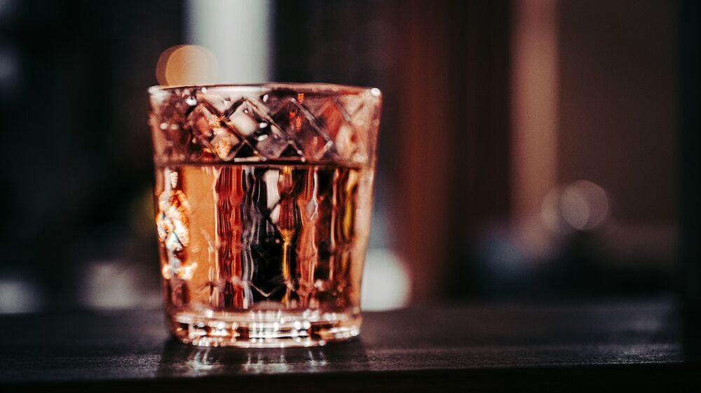 Where a comedian meet and greet happens: a cut-glass tumbler of something amber on a dark bar top, warm lights behind