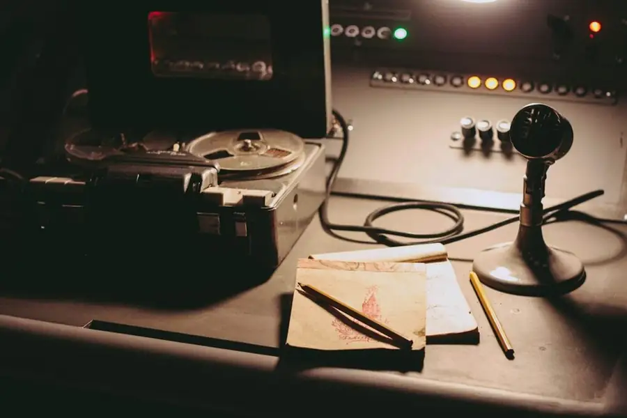 A broadcast desk with a microphone, a reel-to-reel tape machine and notes, for a comic’s guide to the podcast market