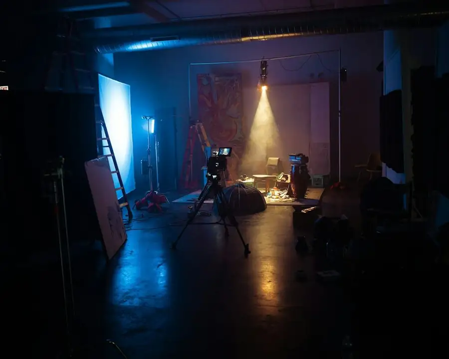 A camera on a tripod filming a small spot-lit set in a dark studio: making a comedy special