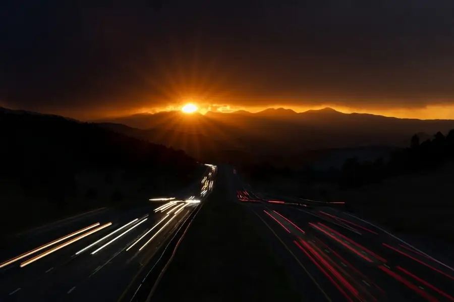 A highway at sunset, headlight and taillight streaks running toward the hills: how far to drive between gigs