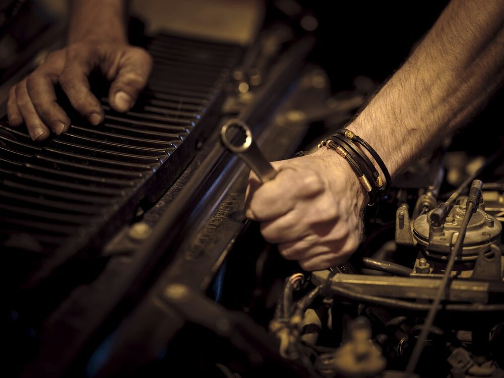 Building it yourself before comedy agents join in: hands working a wrench over an engine bay, in warm tungsten light