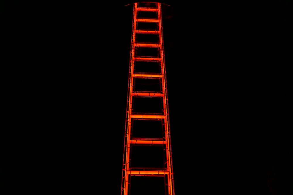 The climb the comedy road maps chart: a ladder outlined in glowing orange light, rising into darkness