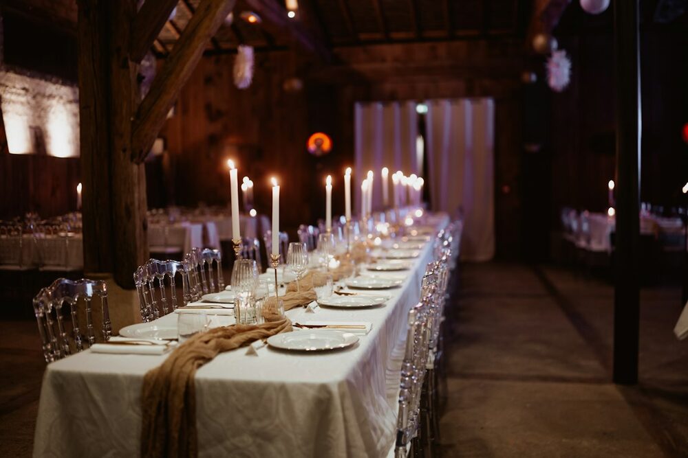 A long party table set with candles and white cloths in a dim timber room, the kind of private event you can hire a comedian for