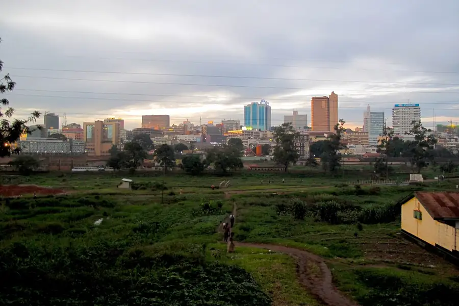 Stand-up comedy in Uganda: the Kampala skyline under an evening sky, seen across open ground and a railyard
