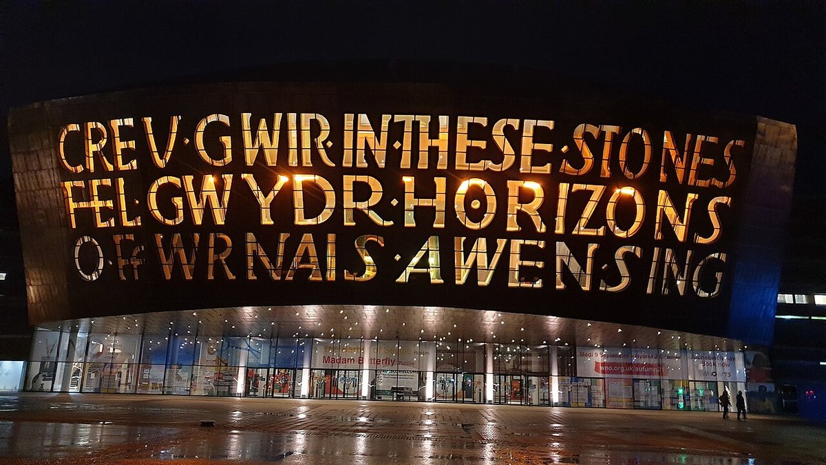 Stand-up comedy in Wales: the Wales Millennium Centre on Cardiff Bay at night, its Welsh and English words lit gold across the front